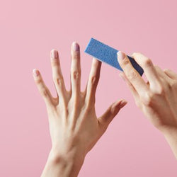 Handpolering av naturliga naglar med en blå 4-vägs nagelbuffer mot rosa bakgrund